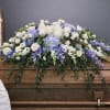 White and blue floral casket spray on a wooden casket