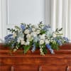 White and blue floral spray arranged on a wooden casket