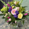 Vase arrangement of pink tulips, purple lisianthus, a yellow rose and mixed blooms in a clear glass vase.