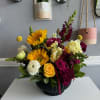 Mixed bouquet with sunflowers, roses, and snapdragons in a black vase