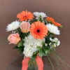 Bouquet of orange gerbera daisies, white mums, and peach roses in a glass vase