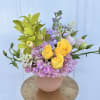 Bouquet of yellow roses, green orchids, and pink hydrangeas in a blush vase