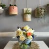 Mixed bouquet in a clear glass vase with cream, peach, blue, and yellow flowers.