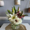Mixed bouquet with white lilies, hydrangeas, and pink blooms in a glass vase