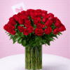 Tall clear vase filled with many red roses and a small card on a white table