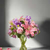 Pink lilies and roses with purple flowers in a clear glass vase