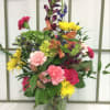 Colorful mixed bouquet in a clear glass vase with pink, yellow, purple, and orange blooms