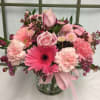Pink mixed flower bouquet in a clear glass vase with a ribbon