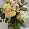 Cream and blush roses mingle with layered white ranunculus and ruffled lisianthus