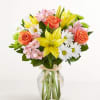 Bouquet of yellow lilies, orange roses, and white daisies in a glass vase