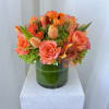 Orange roses and tulips arranged in a green glass vase