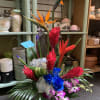 Tropical arrangement with bird of paradise, blue roses, orchids, and red ginger in a vase