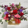 Mixed bouquet of roses, tulips, and purple blooms in a gift box with a ribbon