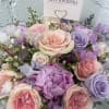 Pastel bouquet of roses and purple blooms with a florist card