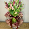 Pink and purple tulips in a round glass vase with a burgundy ribbon