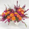 Orange and magenta roses in a white vase with purple filler flowers