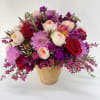 Mixed bouquet of red, pink, and peach flowers in a tan vase