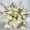 White floral arrangement in a cream vase with roses and orchids