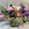 Mixed pink, purple, and white flowers in a clear glass vase