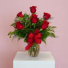 Red rose arrangement in a clear glass vase with a red bow on a white pedestal and pink background