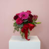 Pink and red flower bouquet in a glass vase with a red ribbon