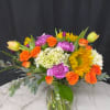 Colorful bouquet of orange roses, sunflowers, and purple carnations in a glass vase