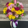 Mixed pink, yellow, and purple bouquet in a white vase with a purple ribbon