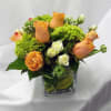 Orange roses and green blooms arranged in a square glass vase