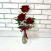 Three red roses in a clear glass vase with baby's breath and a red ribbon