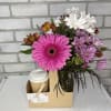 Mixed bouquet with bright pink gerbera daisy in glass vase next to a to-go coffee cup in a cardboard caddy.