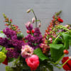 Tall mixed arrangement with purple lilacs, pink fringe tulips, and red blooms in a glass vase.