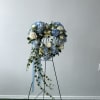 Heart-shaped floral wreath with blue hydrangeas and white roses on a stand