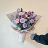 Hand-tied bouquet of lavender roses and pink flowers wrapped in paper