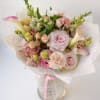 Bouquet of pale pink and white flowers wrapped in white paper with a pink ribbon