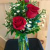 Three red roses with small white daisies in a glass vase
