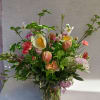Tall garden-style arrangement of pink, peach, and white flowers with branches in a clear glass vase.