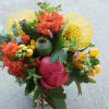 Bright mixed bouquet with yellow pincushion protea, orange blooms, and a pink peony in a glass vase
