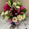 Compact arrangement of pink lilies, roses, and green carnations in a blue vase with a pink ribbon bow