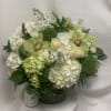 Round arrangement of white hydrangeas, cream roses, and green orchids in a clear glass vase