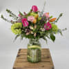 Mixed bouquet of pink roses, orange lilies, and green hydrangeas in a clear glass jar vase