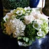 White floral arrangement in a clear glass vase with hydrangeas and roses