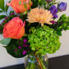 Mixed bouquet with coral roses, purple lisianthus, and a peach chrysanthemum in a glass vase
