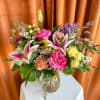 Bouquet of pink lilies, roses, and yellow blooms in a glass vase