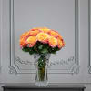 Orange and pink roses arranged in a clear glass vase with a striped ribbon