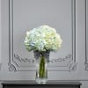 White and pale blue hydrangeas in a clear vase with a striped ribbon