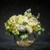 White and pale green floral arrangement in a round glass vase with stones