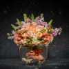 Peach roses and orchids arranged in a round glass vase with stones