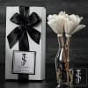 White gift box with black ribbon beside white flowers in a glass vase