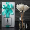 White flowers in a clear glass vase beside a gift box with a teal ribbon.