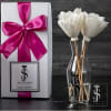 White flowers in a clear vase beside a gift box with a pink ribbon